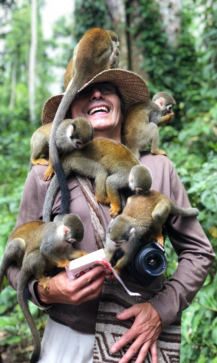A smiling person with squirrel monkeys on their shoulders in the Amazon jungle, showcasing wildlife interaction.